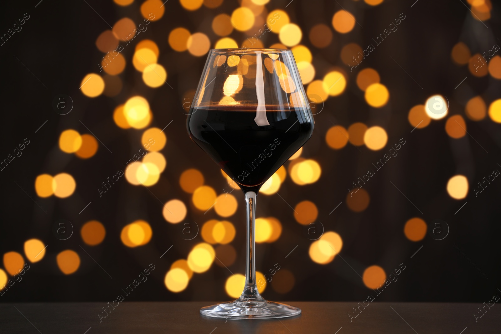 Photo of Tasty red wine in glass on table against dark background with blurred lights, bokeh effect