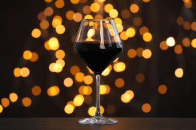 Photo of Tasty red wine in glass on table against dark background with blurred lights, bokeh effect