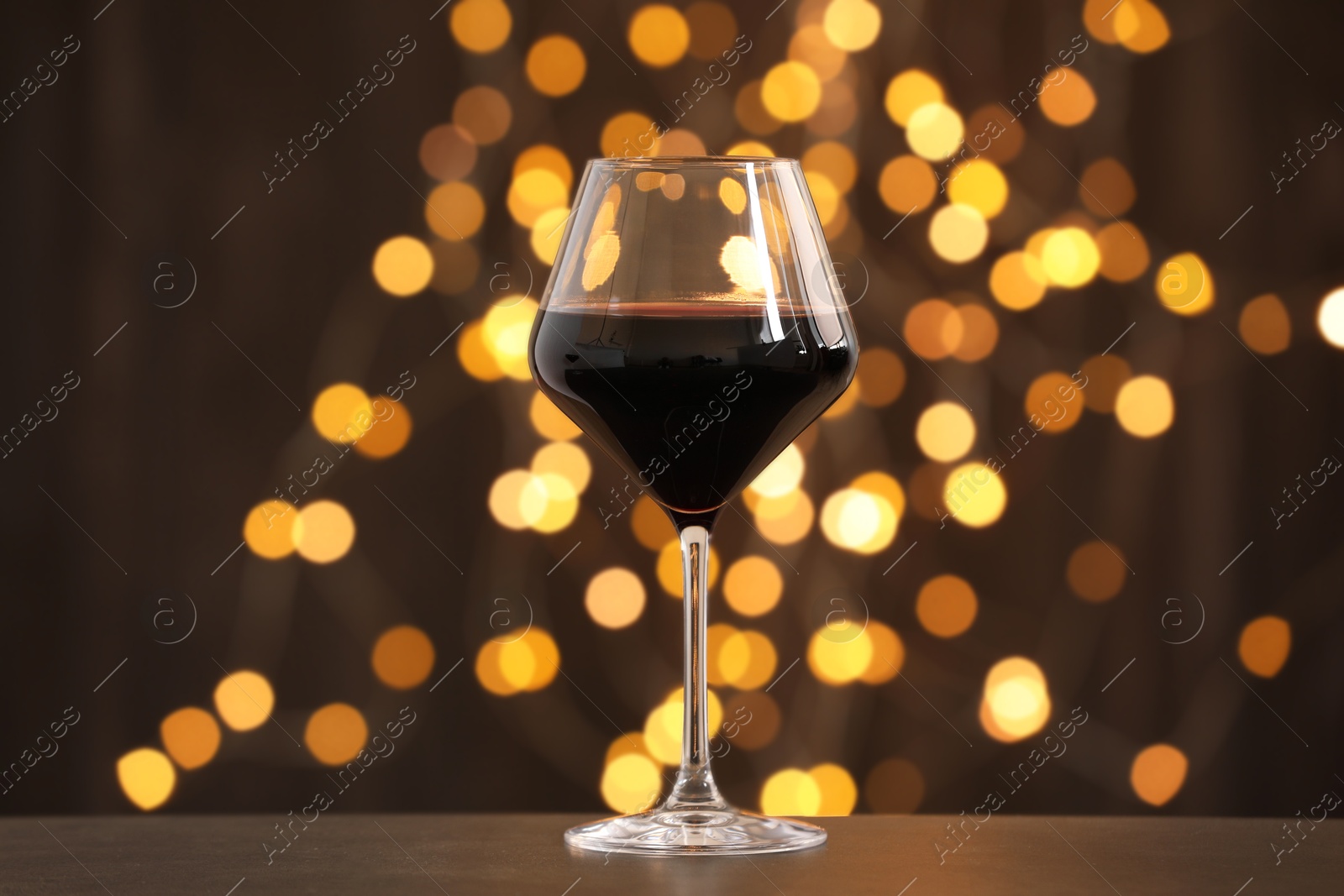 Photo of Tasty red wine in glass on table against dark background with blurred lights, bokeh effect