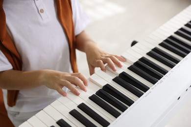 Photo of Boy playing synthesizer indoors, closeup. Electronic musical instrument