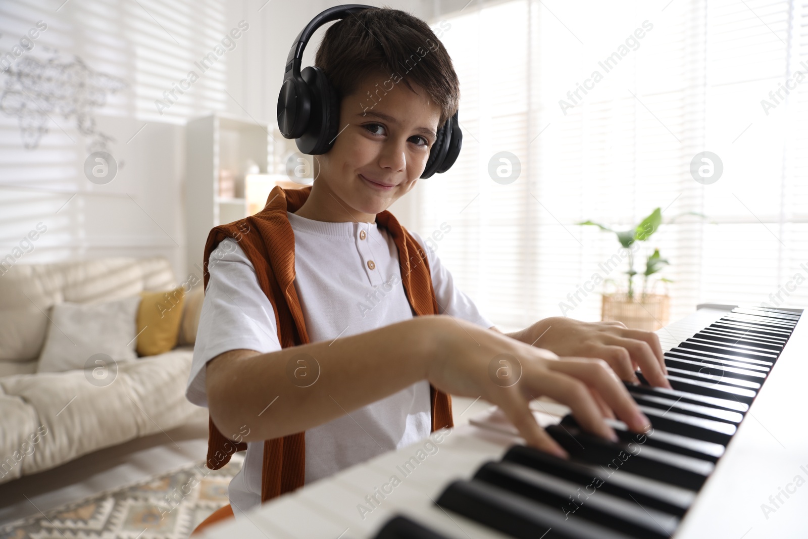 Photo of Cute boy in headphones playing synthesizer at home