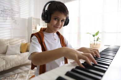 Photo of Cute boy in headphones playing synthesizer at home