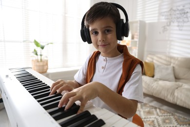 Cute boy in headphones playing synthesizer at home