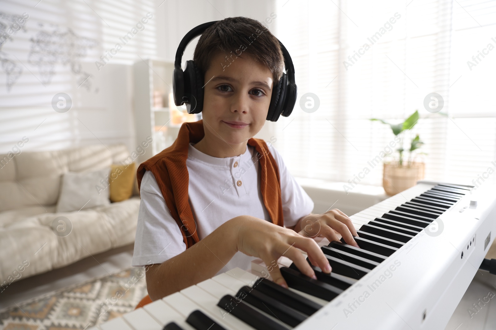 Photo of Cute boy in headphones playing synthesizer at home