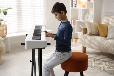 Photo of Little boy playing synthesizer at home. Electronic musical instrument