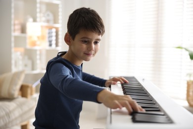 Photo of Cute boy playing synthesizer at home. Electronic musical instrument