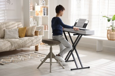 Photo of Little boy playing synthesizer at home. Electronic musical instrument