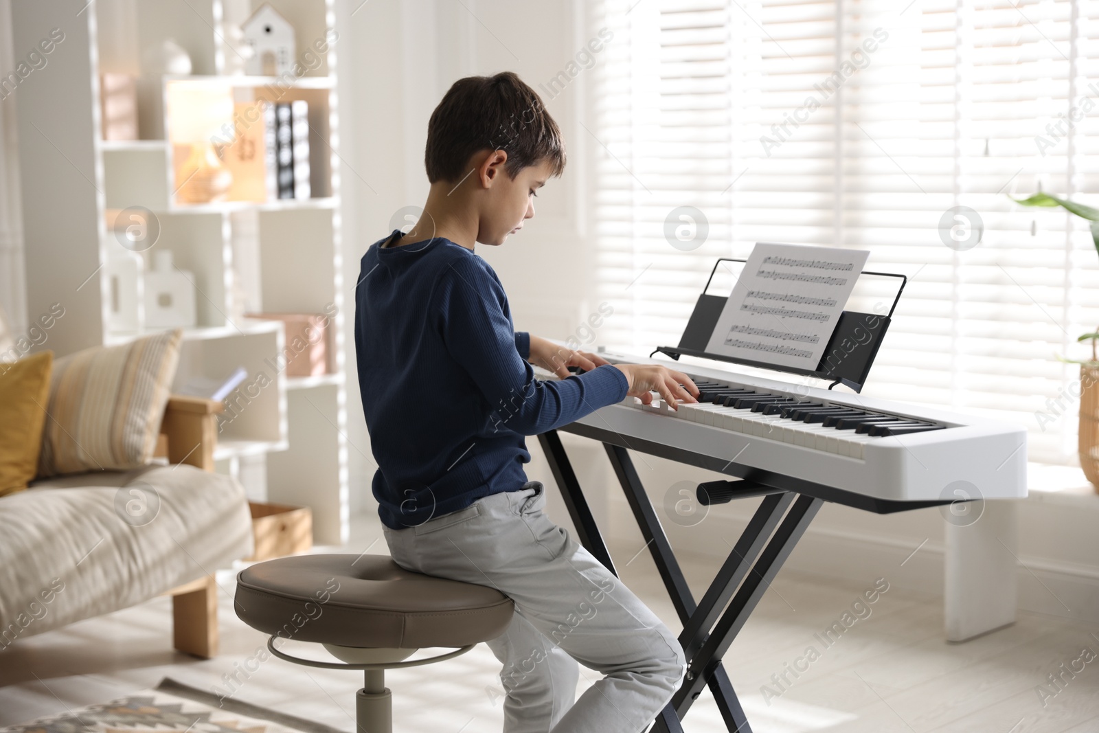 Photo of Little boy playing synthesizer at home. Electronic musical instrument