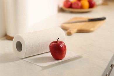 Photo of Roll of paper towels and red apple on white countertop in kitchen, space for text