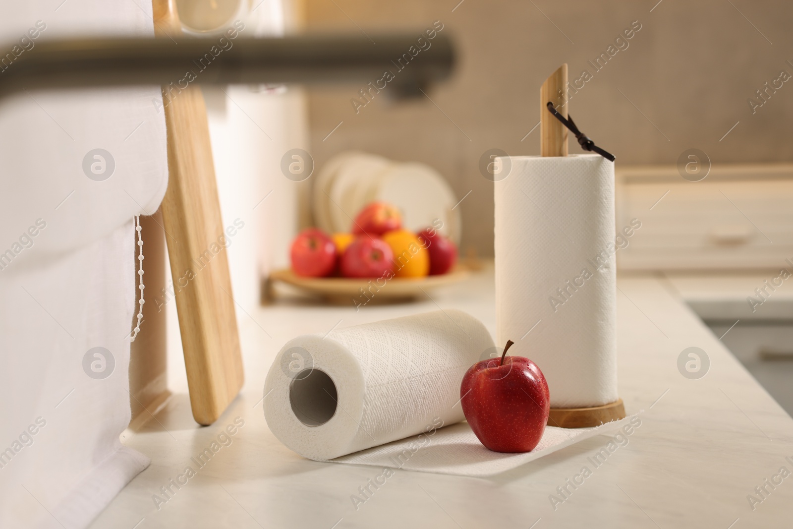 Photo of Rolls of paper towels and red apple on white countertop in kitchen