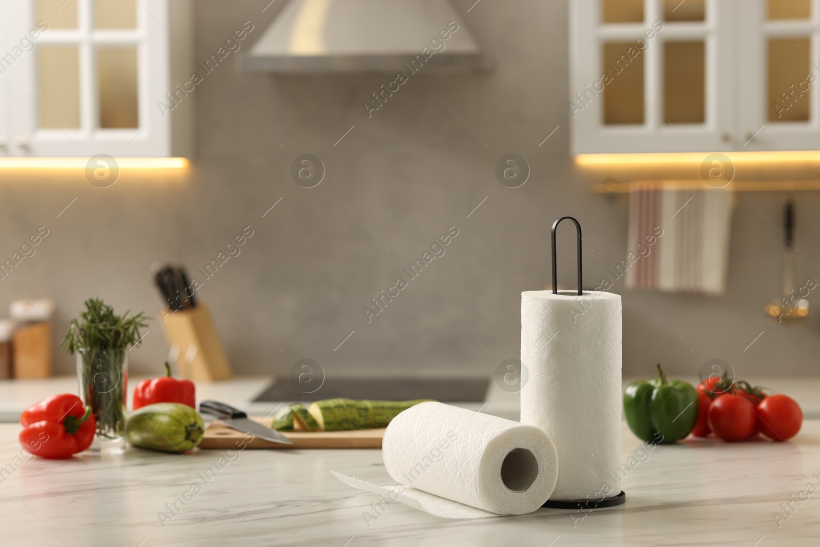 Photo of Rolls of paper towels and vegetables on white marble table in kitchen