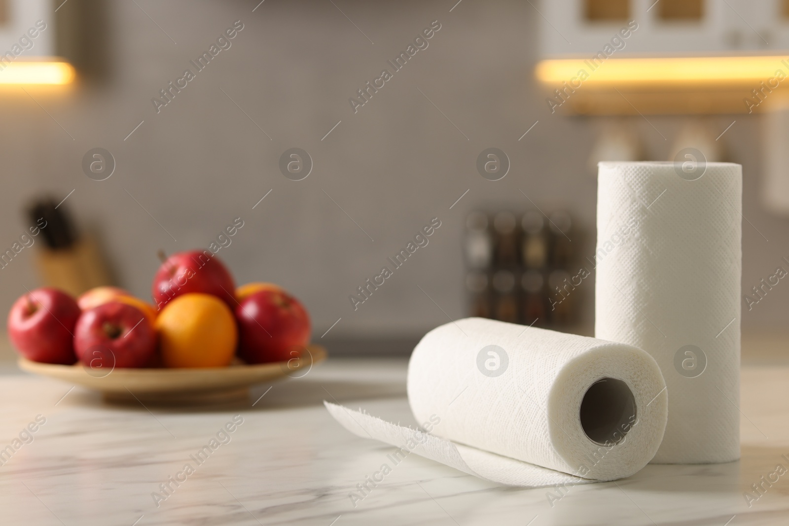 Photo of Rolls of paper towels and fruits on white marble table in kitchen