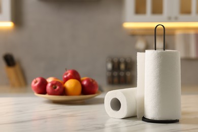 Photo of Rolls of paper towels and fruits on white marble table in kitchen