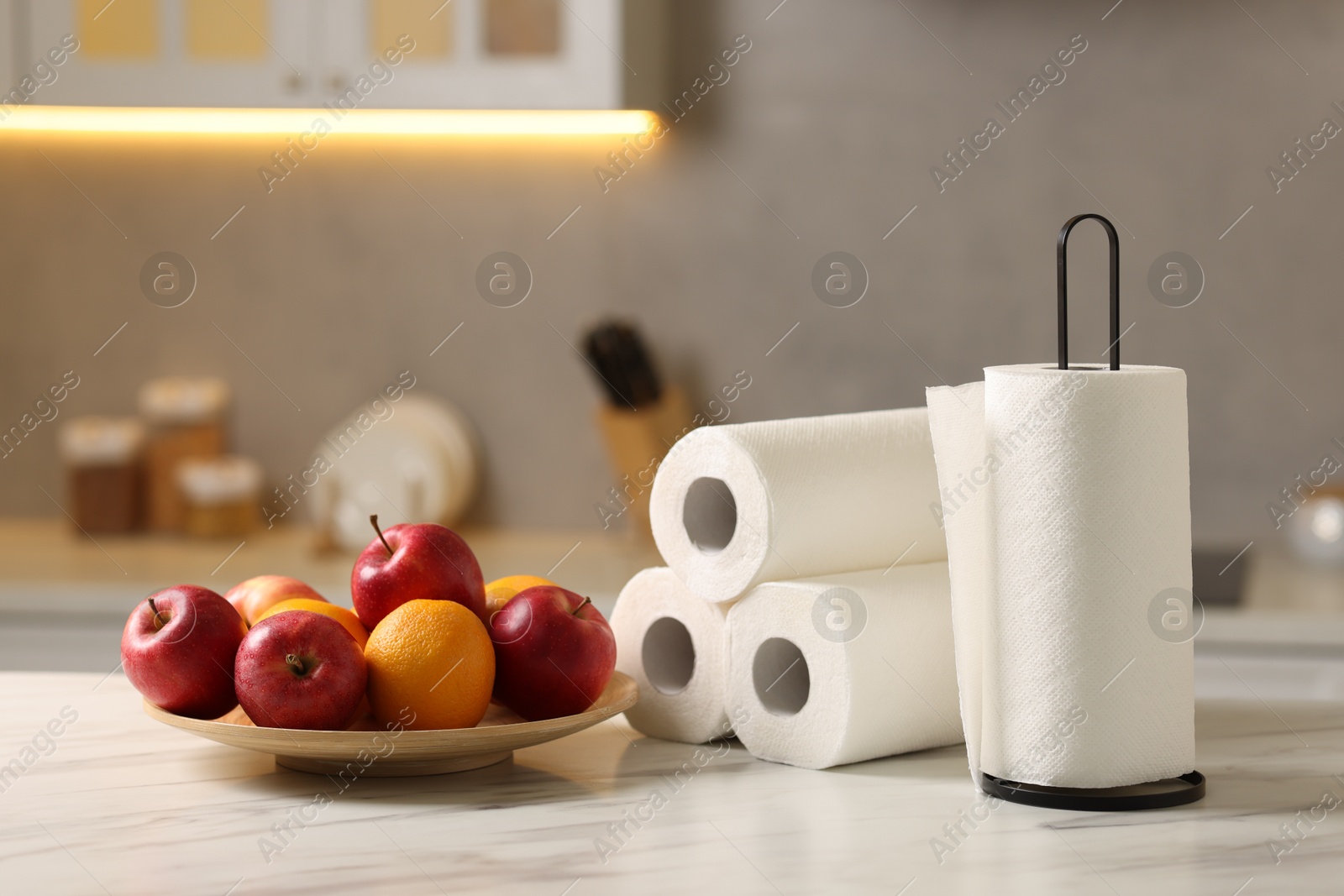 Photo of Rolls of paper towels and fruits on white marble table in kitchen