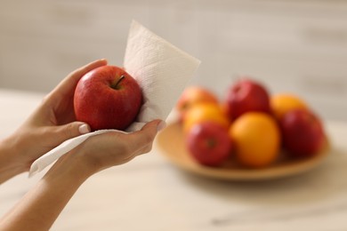 Photo of Woman wiping apple with paper towel in kitchen, closeup