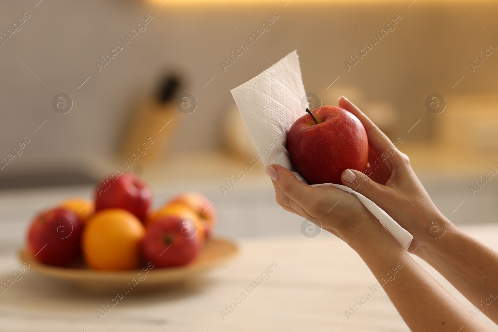 Photo of Woman wiping apple with paper towel in kitchen, closeup