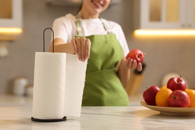 Photo of Woman with apple using paper towels at white marble in kitchen, closeup