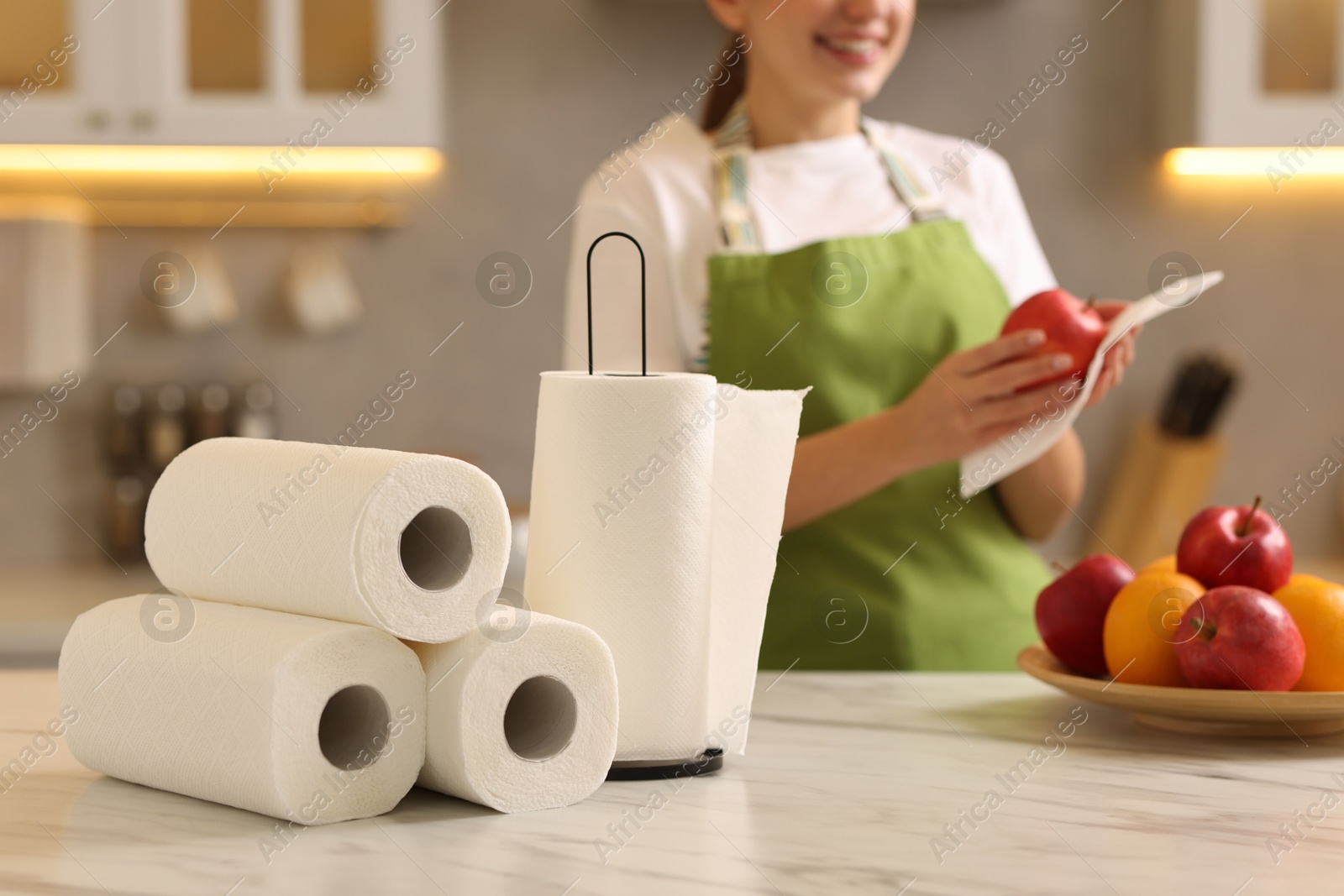 Photo of Woman wiping apple with paper towel at white marble table in kitchen, focus on rolls