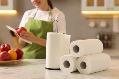 Photo of Woman wiping apple with paper towel at white marble table in kitchen, focus on rolls