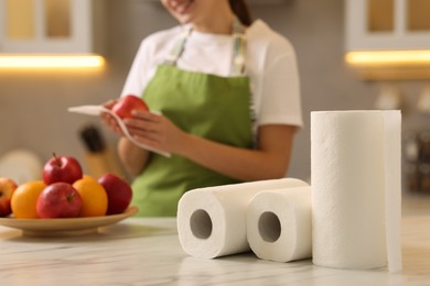 Photo of Woman wiping apple with paper towel at white marble table in kitchen, focus on rolls