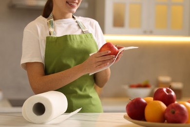 Photo of Woman wiping apple with paper towel at white marble table in kitchen, closeup