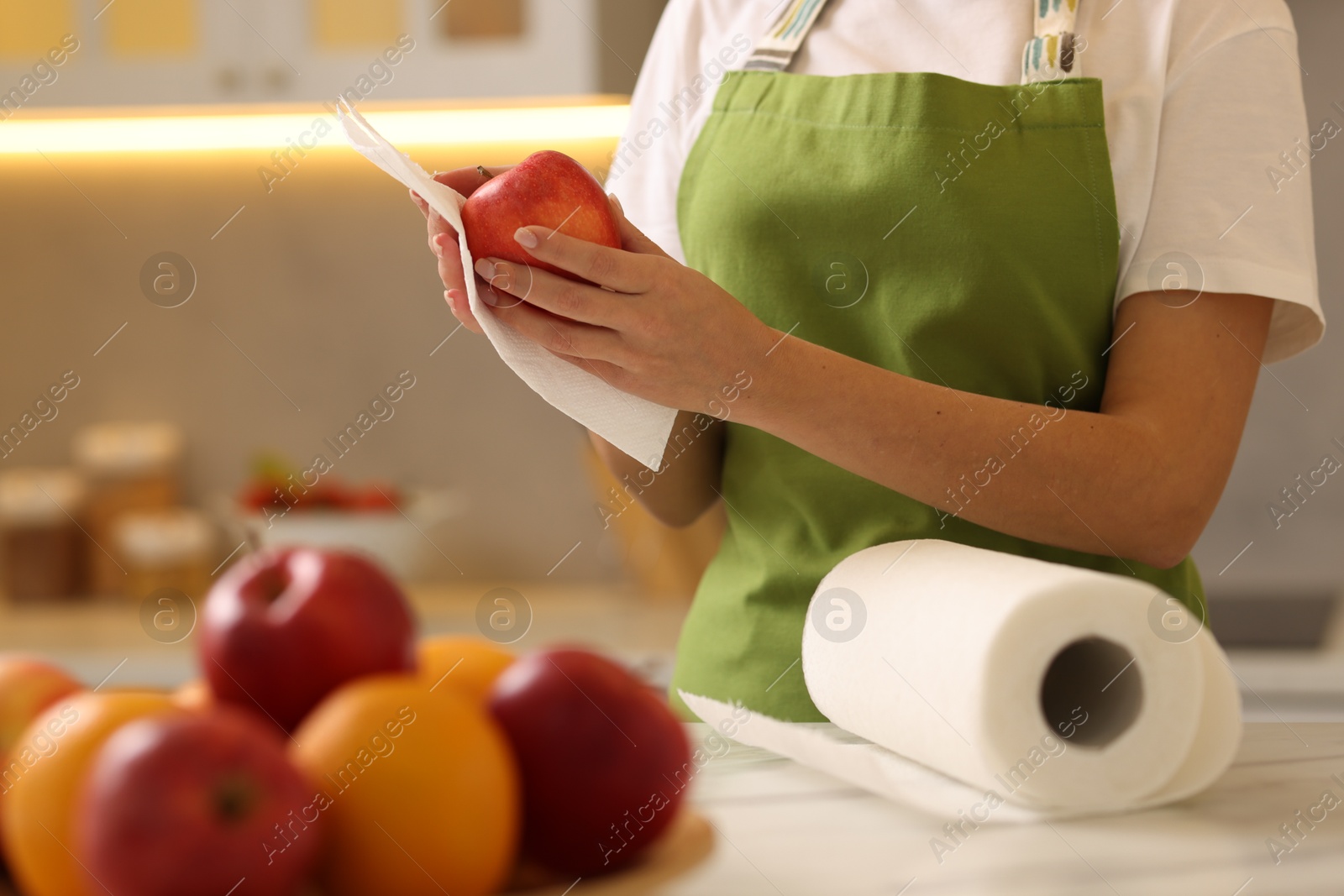 Photo of Woman wiping apple with paper towel at white marble table in kitchen, closeup