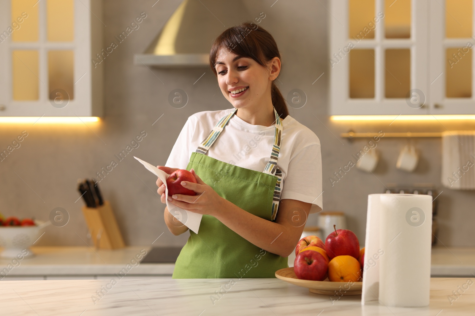 Photo of Woman wiping apple with paper towel at white marble table in kitchen