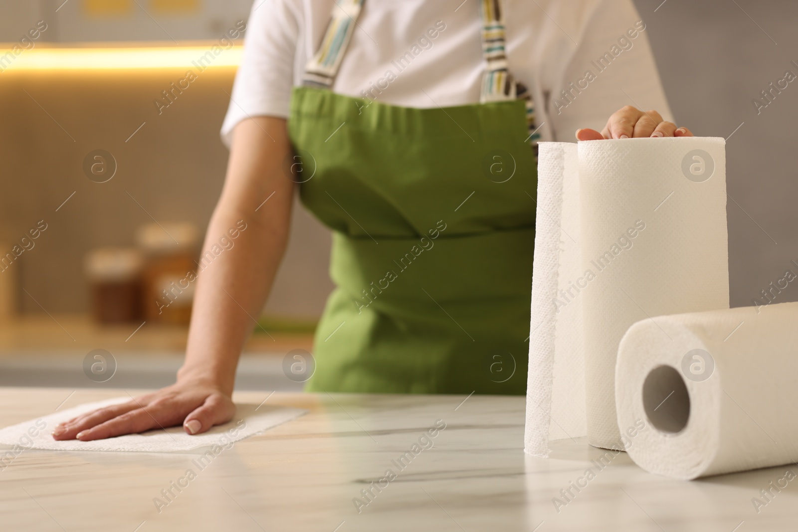 Photo of Woman cleaning white marble table with paper towel in kitchen, closeup