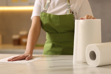 Photo of Woman cleaning white marble table with paper towel in kitchen, closeup