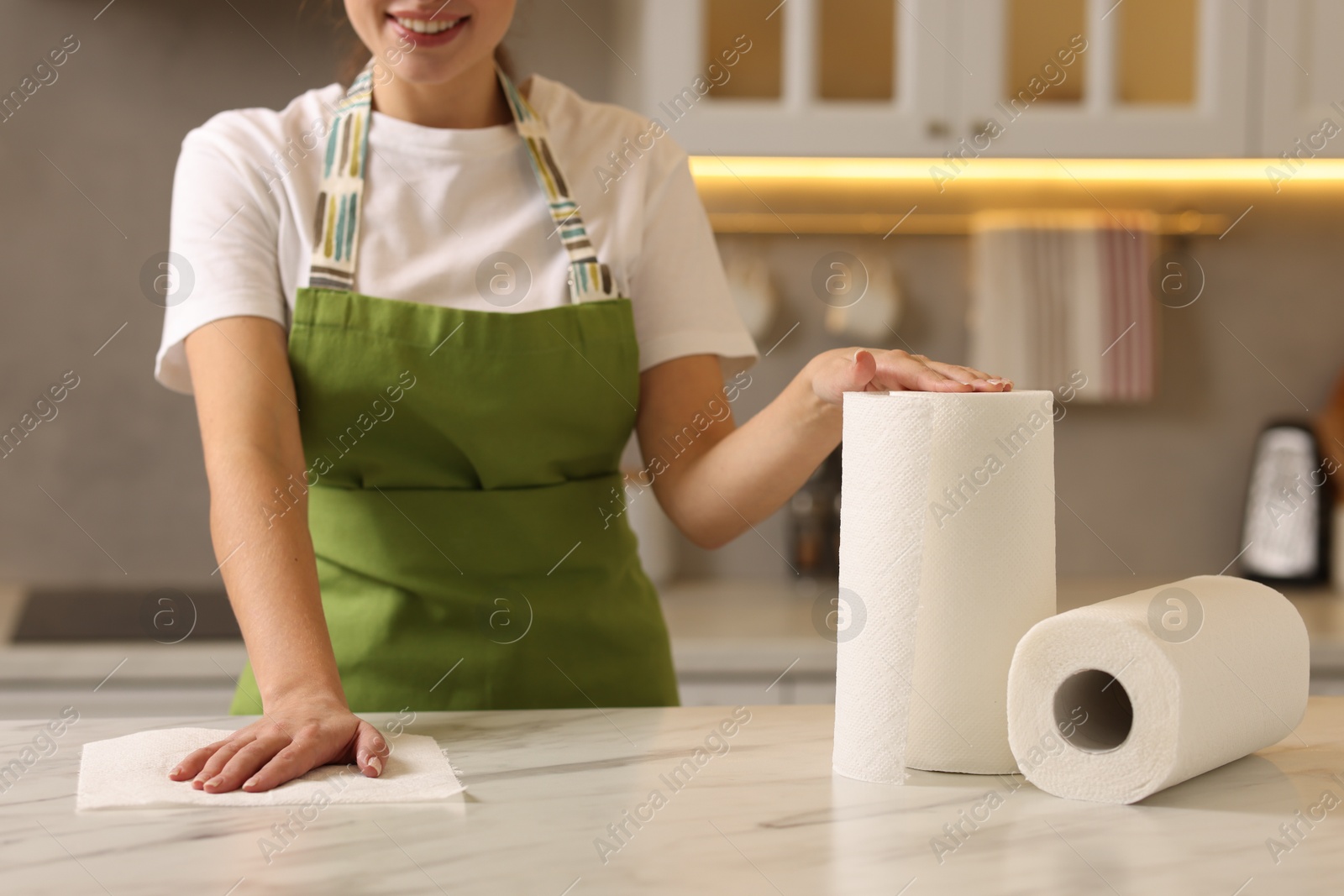 Photo of Woman cleaning white marble table with paper towel in kitchen, closeup