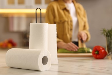 Photo of Woman cutting zucchini at white marble table in kitchen, focus on rolls of paper towels