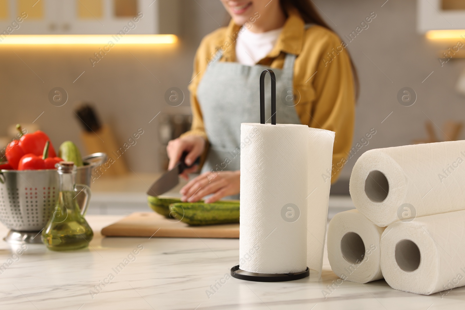 Photo of Woman cutting zucchini at white marble table in kitchen, focus on rolls of paper towels