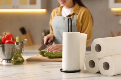 Photo of Woman cutting zucchini at white marble table in kitchen, focus on rolls of paper towels