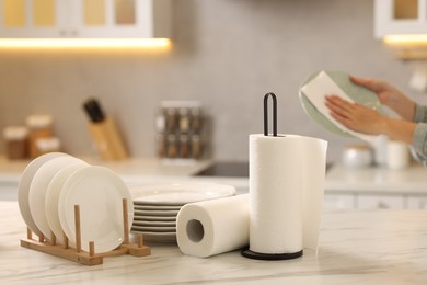 Photo of Woman wiping plate with paper towel at white marble table in kitchen, closeup