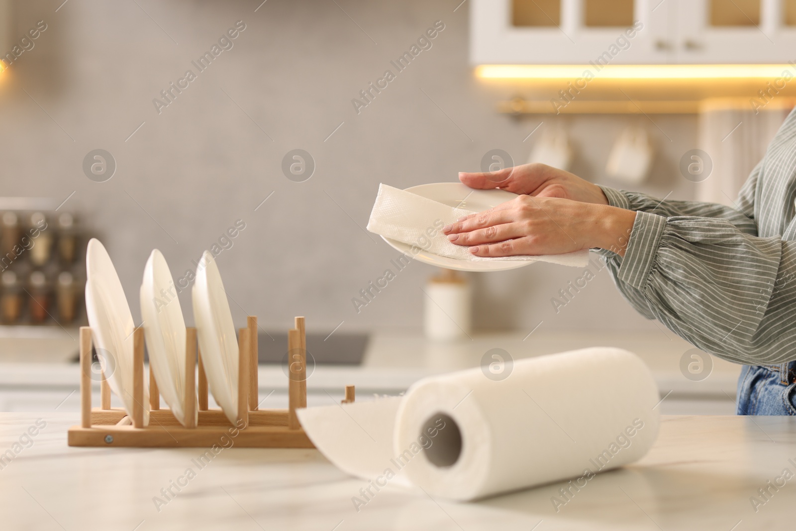 Photo of Woman wiping plate with paper towel at white marble table in kitchen, closeup