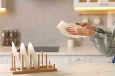 Photo of Woman wiping plate with paper towel at white marble table in kitchen, closeup