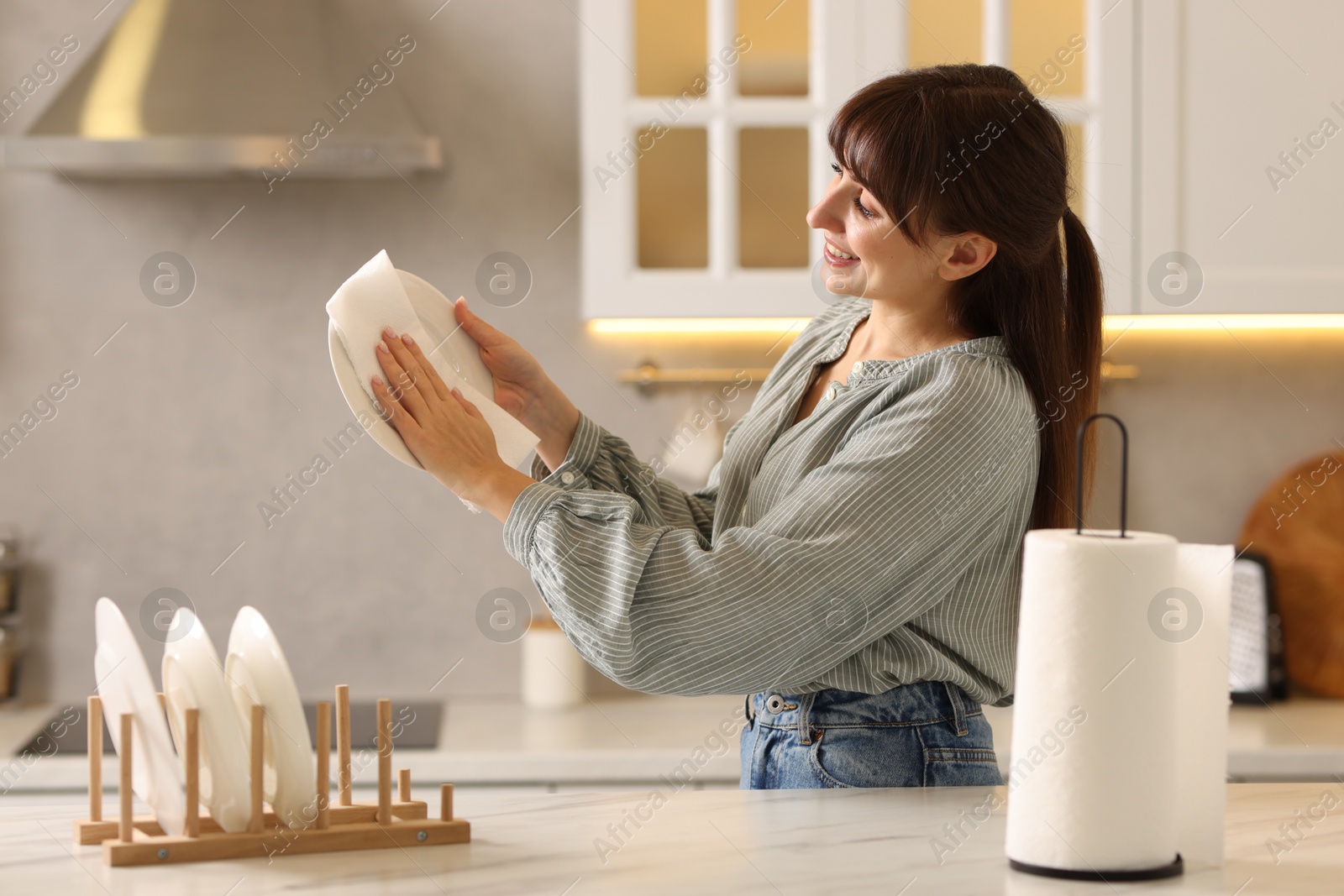 Photo of Woman wiping plate with paper towel at white marble table in kitchen