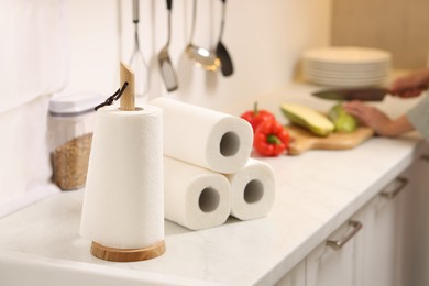 Photo of Woman cutting vegetables at white countertop in kitchen, focus on rolls of paper towels