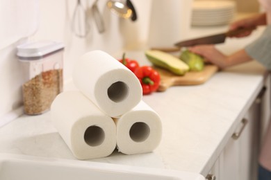 Photo of Woman cutting vegetables at white countertop in kitchen, focus on rolls of paper towels