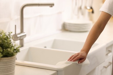 Photo of Woman cleaning sink with paper towel in kitchen, closeup