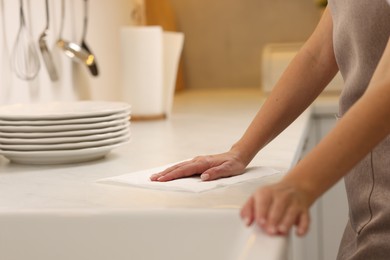 Photo of Woman cleaning countertop with paper towel in kitchen, closeup