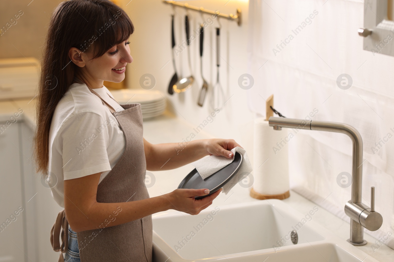 Photo of Smiling woman wiping plate with paper towel above sink in kitchen