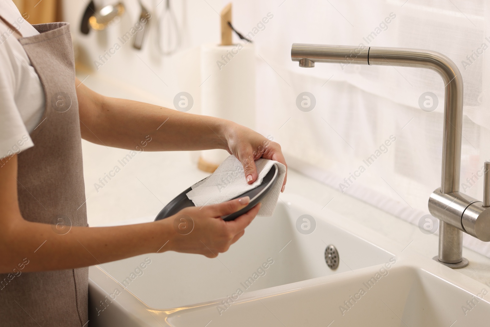 Photo of Woman wiping plate with paper towel above sink in kitchen, closeup