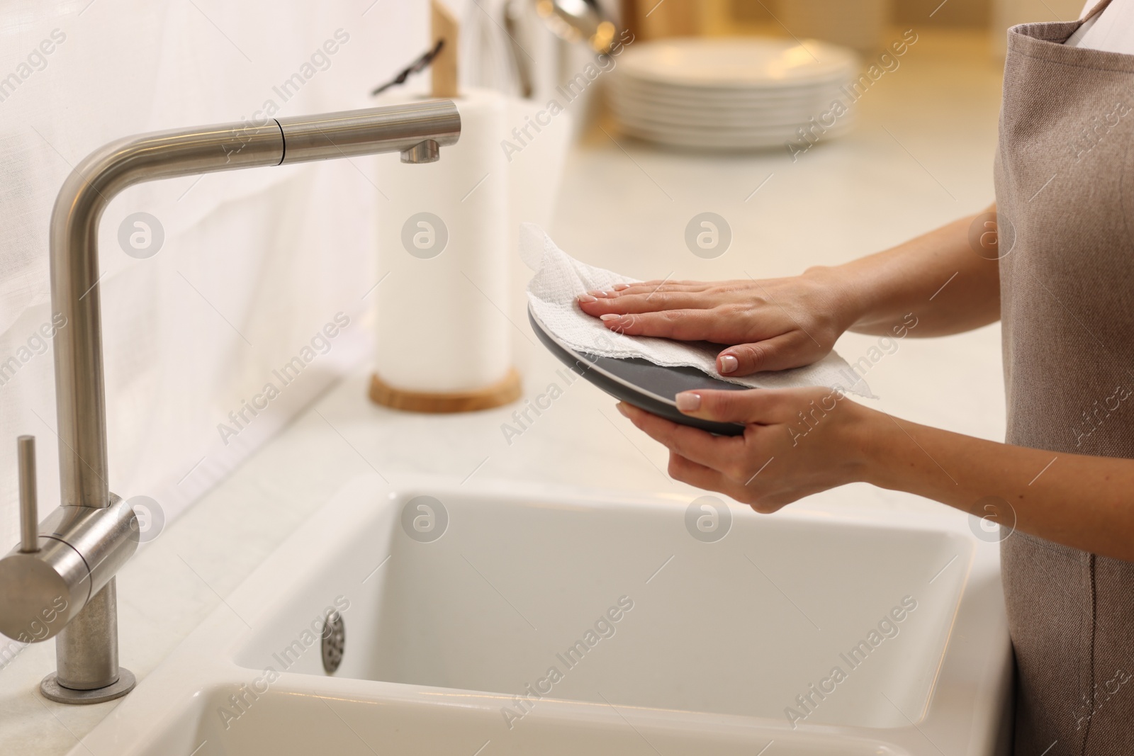 Photo of Woman wiping plate with paper towel above sink in kitchen, closeup