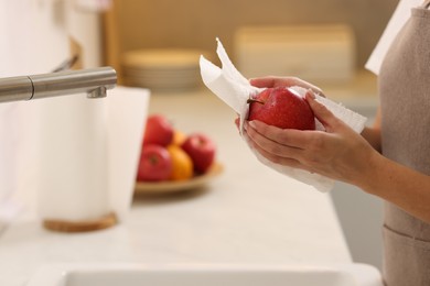 Photo of Woman wiping apple with paper towel in kitchen, closeup