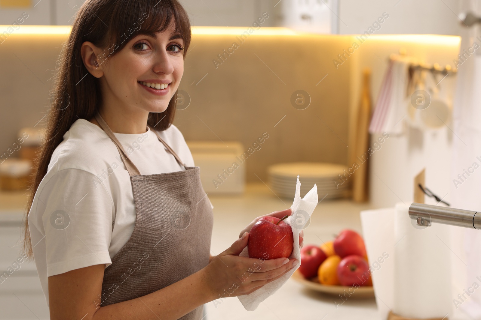 Photo of Smiling woman wiping apple with paper towel in kitchen