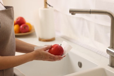 Photo of Woman wiping apple with paper towel above sink in kitchen, closeup