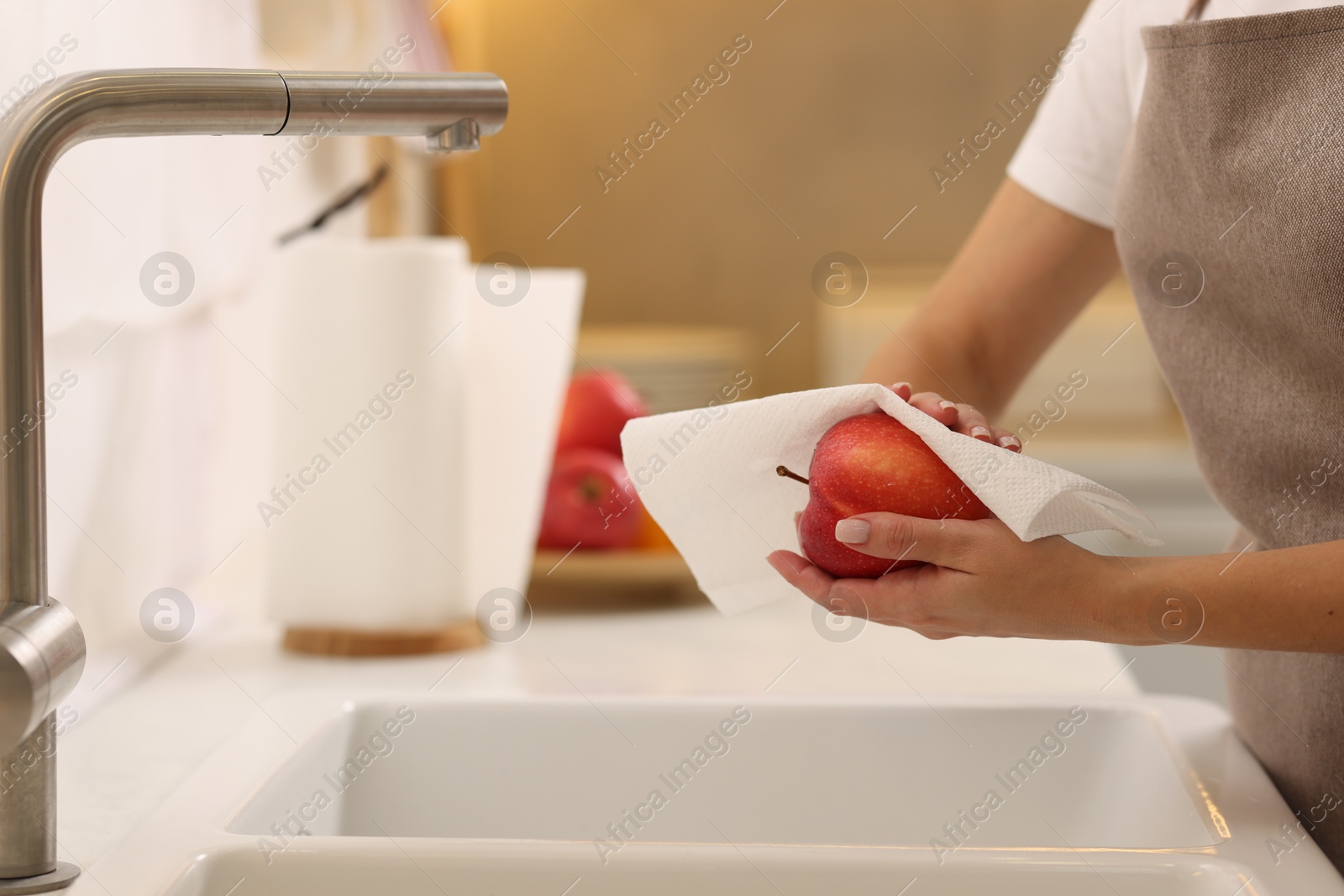 Photo of Woman wiping apple with paper towel above sink in kitchen, closeup