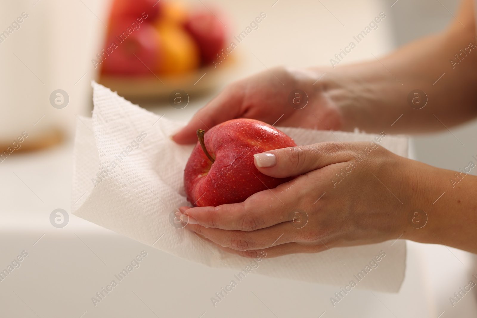 Photo of Woman wiping apple with paper towel in kitchen, closeup