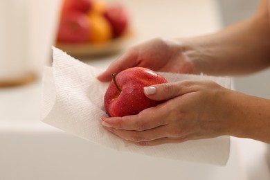 Photo of Woman wiping apple with paper towel in kitchen, closeup